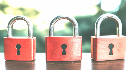 Naklejka premium Three Red Padlocks on Wooden Surface with Blurred Green Background