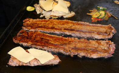 sausage open on the hot grill cooking with other meat and melted cheese