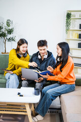 Three Asian young adult students sit in university living room, discussing their study abroad...