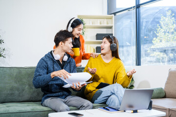 Three Asian young adult students sit in university living room, discussing their study abroad...