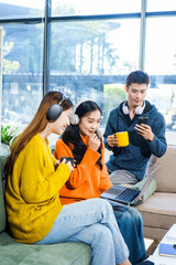 Three Asian young adult students sit in university living room, discussing their study abroad experiences, academic research, preparing thesis report, planning future global education opportunities.