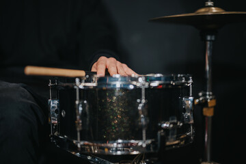 A musician's hand resting on a shiny snare drum with drumsticks nearby, emphasizing music and...