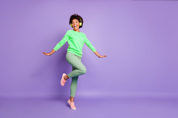 Full length body size turned photo of cheerful positive cute nice charming girlfriend dancing in headphones wearing yellow sweater green pants trousers isolated over violet pastel color background