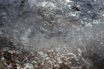 Close-up of ice-covered ground with trapped air bubbles and sunlight reflections. A natural winter texture showcasing frozen water patterns and details