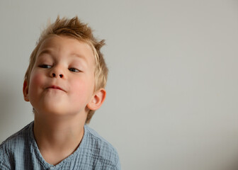 A cheerful little boy with a mischievous smile, tousled blonde hair, and a playful facial...