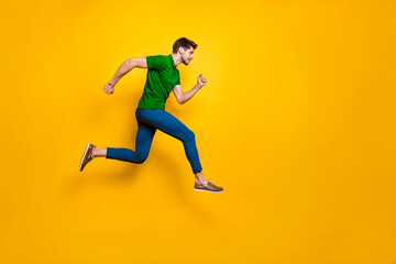 Fototapeta na wymiar Full length body size side profile photo of fast quick handsome man wearing blue pants trousers footwear running jumping to empty space isolated over vivid color background