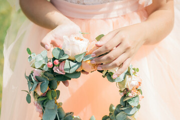 A beautifully styled floral crown with pastel roses, greenery, and delicate berries, gently held by...