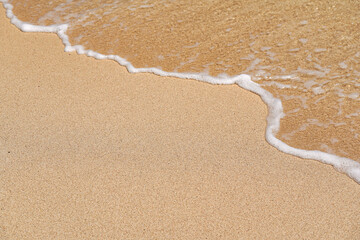 Sandy beach, lit by sun, sea water washes over, closeup detail - abstract shallow depth of field tropical vacation background