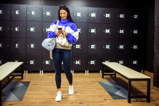 Woman goes out of the dressing room of the gym with her sports bag and phone.