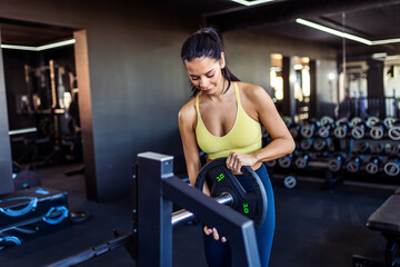 Young fit woman putting weights on a bar in the gym.