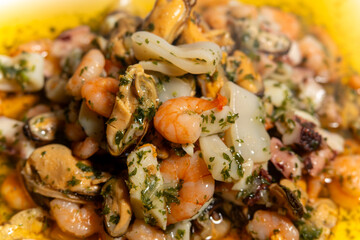 A delicious seafood dish featuring shrimp, squid, and clams is served on a yellow plate. The shrimp are arranged on top of the clams and squid, creating a visually appealing presentation
