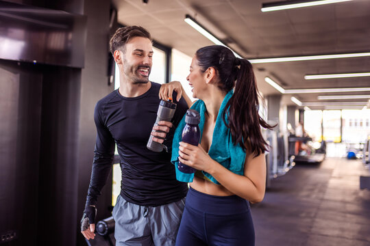 Two gym partners walk through the gym with water bottles and towel.