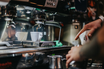 An espresso is being prepared by flowing from a coffee machine into a cup by a barista.