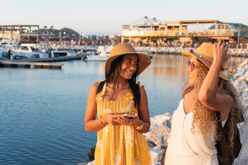 Two tourists smiling and talking at marina during sunset