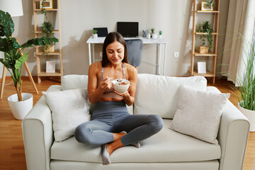 Obraz premium Healthy lifestyle concept with fit sportswoman eating cereals for breakfast in her living room