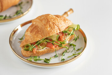 Croissant sandwich with salmon, onions and microgreens on white table. Healthy breakfast. Front view