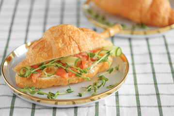 Croissant sandwich with salmon, onions and microgreens on white table. Healthy breakfast. Front view