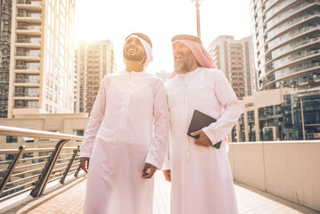 Senior and young arabian men wearing kandura traditional dress from uae in Dubai. Speaking about...