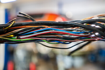 A bundle of colorful electrical wires exposed in a vehicle workshop, showing intricate automotive...