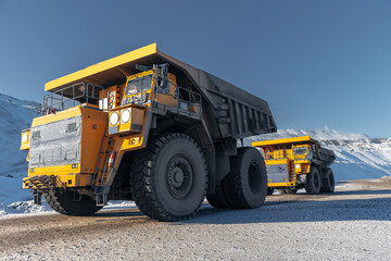Big yellow dump trucks in snowy open pit coal mine during winter day