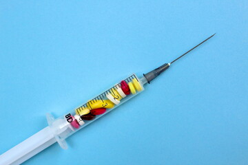 On a blue background lies a syringe inside which are tablets	