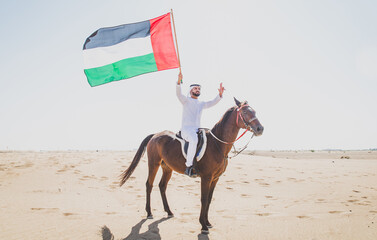 Young adult with Kandura, the emirates traditional clothes, riding his horse in the desert