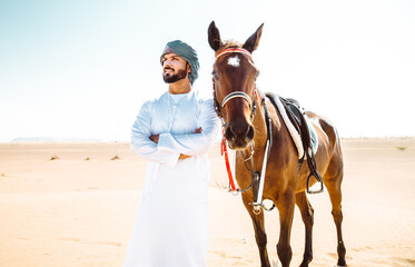 Young adult with Kandura, the emirates traditional clothes, riding his horse in the desert