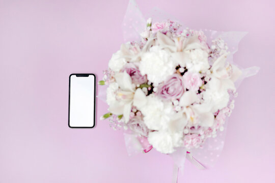 A phone with a white screen lies near the flowers isolated on pink background. The concept of online shopping. A gift for beloved woman. International Women's Day. Concept of love