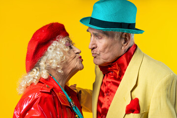 Beautiful senior old couple wearing fancy party clothes acting in studio on a colored background....