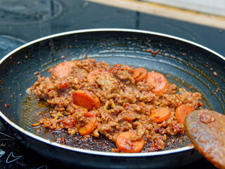 Sizzling ground meat with sliced vegetables cooking in a round pan on the stove.