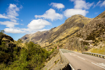 Road going through the Glen Coe Valley with the rugged Grampian Mountains rising up next to it
