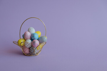 On the left side there is a basket with Easter colorful eggs, on the right side there is a place for text, congratulations or advertising. On a purple background . Easter Holiday Concept