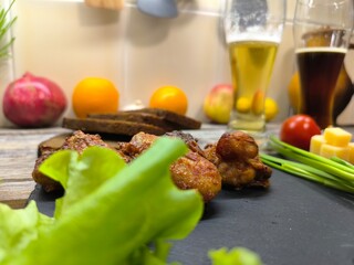 Fried chicken pieces lie on a sliced board next to glasses of beer