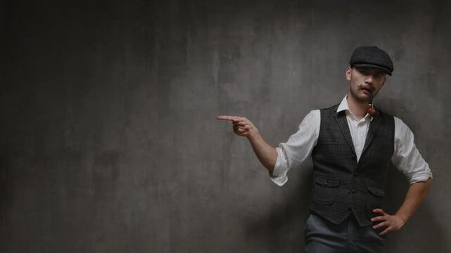 Young handsome confident rude mustachioed man in vintage suit, cap pointing the finger on copy space in front of concrete wall. Commercial product promotion template for mens theme
