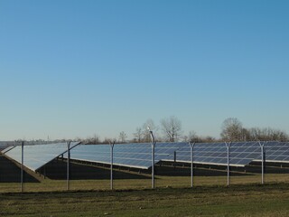 Rows of solar panels in a fenced area under a clear blue sky at a solar power plant outside the city, collecting and accumulating solar energy on an industrial scale