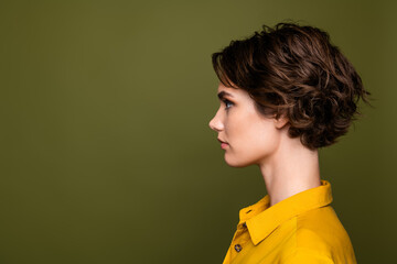 Side profile of a stylish young woman with short brunette hair wearing a yellow shirt against a...