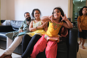 Happy indian family having fun at home - Asian parents and children wearing sari dress during religious event - Culture and family love concept