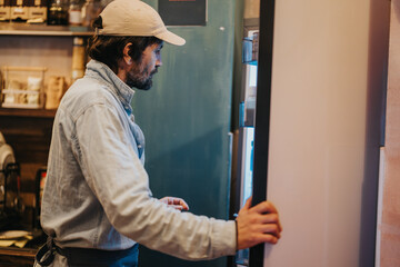 A man in casual clothing inspects the contents of a refrigerator in a warm, rustic setting, evoking a sense of curiosity and comfort.