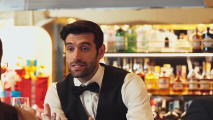 Good looking bartender warm smiling friendly conversation with couple customer at beverage bar counter while serving welcome drink with charm professionalism recommending special menu list. Vinosity.
