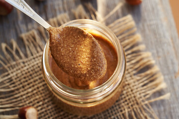 Homemade hazelnut butter on a metal spoon above a glass jar