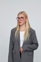 A young woman in a gray jacket and oversized glasses. Burgundy eyeglass frame. Stylish business outfit. Blonde model looks