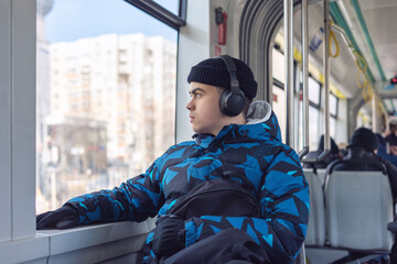 A teenager is riding public transport, listening to music through headphones, and thoughtfully...