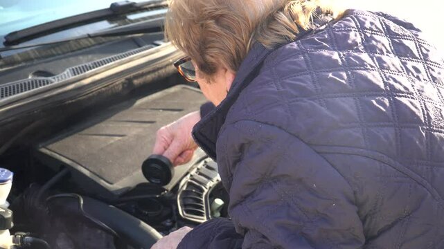 A lady checks the inside of her car's engine while carrying out maintenance and conservation tasks on the car.