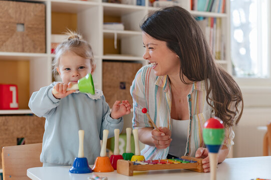 A smiling young woman and a little girl engage in a fun educational activity, playing with musical toys in a bright, cheerful indoor setting