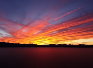 Fototapeta premium Striking sunset over serene lake with fiery sky and mountain silhouette
