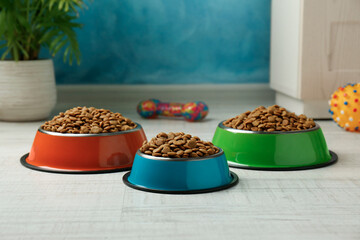 Dry pet food in feeding bowls and toys on floor indoors