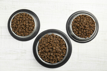 Dry pet food in feeding bowls on floor, flat lay