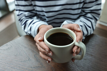 Woman having coffee break at wooden table in cafe, closeup