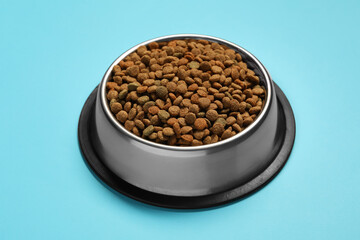 Dry pet food granules in feeding bowl on light blue background