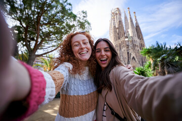 Two happy women friends taking a selfie in front of the sagrada familia, enjoying their vacation...